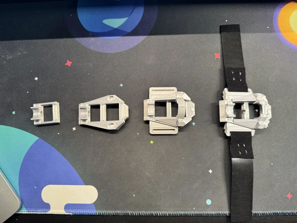 Four grey casing prints, left to right from a small test frame to the final casing on its black Velcro strap.