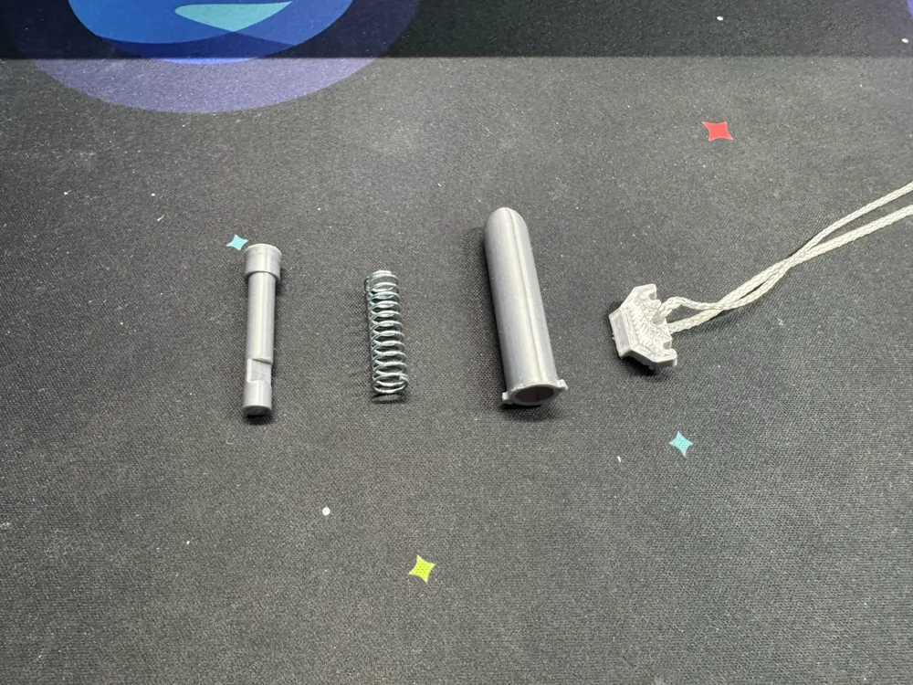 Four parts laid out left to right: the bullet rod, the compression spring, the cartridge tube, and the stopper with its pull string.