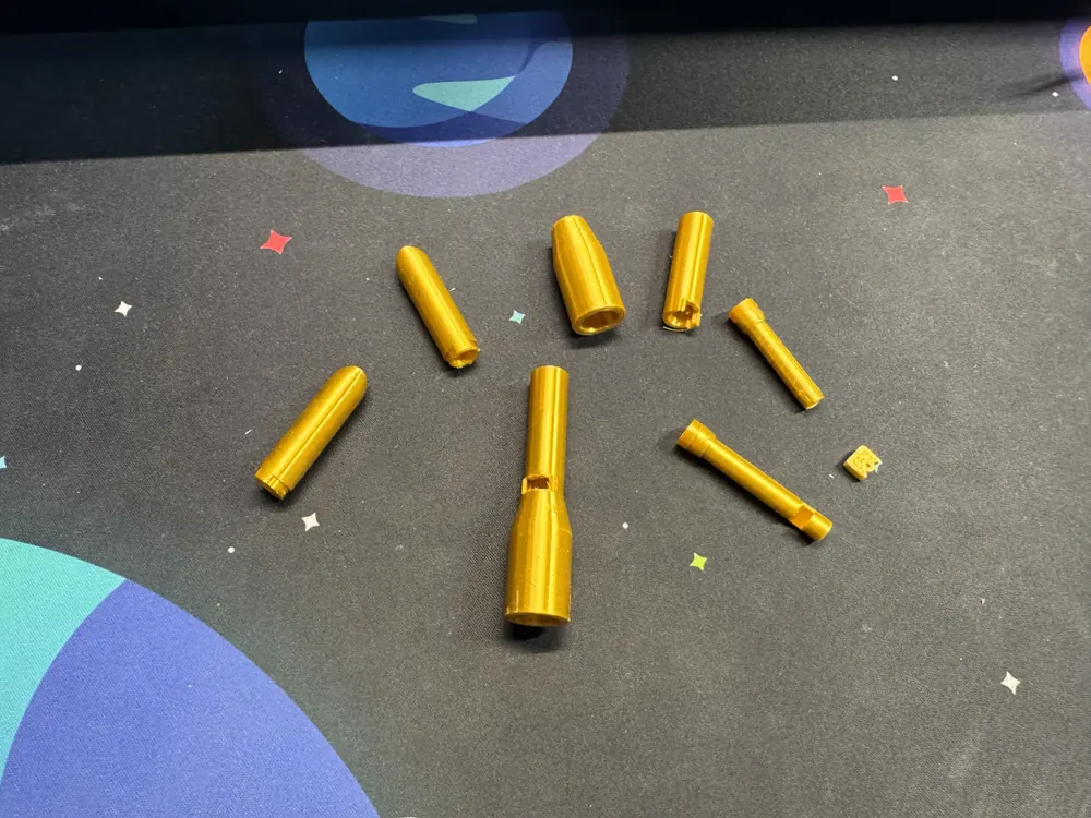 Gold 3D-printed parts from the freshman-year build laid out in an arc on a desk mat.